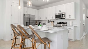 A modern kitchen with white cabinetry, stainless steel appliances, and a central island with bar stools. - Lake View Villa Sleeps 8! (Davenport)