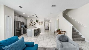 A modern kitchen with a central island, a dining area with a table and chairs, a living room with a sofa and a chair, and a staircase. - Roomy Family Home-sleeps 16 109 (Kissimmee)