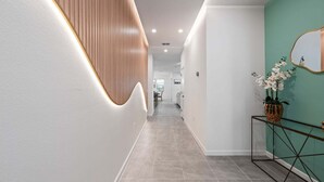 Un pasillo moderno con un panel de madera curvada, una mesita de cristal con una planta y una pared de acento color verde azulado.