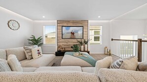 Una sala de estar con un televisor grande, dos sofás, una mesa de centro y una pared de acento de madera.