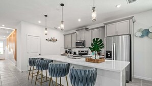 Una cocina moderna con una isla central, taburetes de bar, electrodomésticos de acero inoxidable e iluminación colgante.