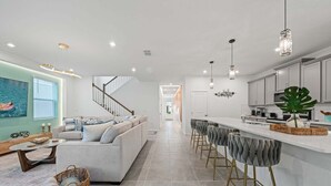 Una cocina moderna con barra, una escalera que lleva a otro nivel y una sala de estar con sofá y mesa de centro.