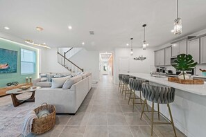 Eine moderne Küche mit Barbereich, einer Treppe zu einer weiteren Ebene und einem Wohnzimmer mit Sofa und Couchtisch.