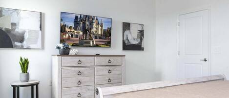 Un dormitorio con una cama, un aparador, una mesita con una planta y tres cuadros en la pared.