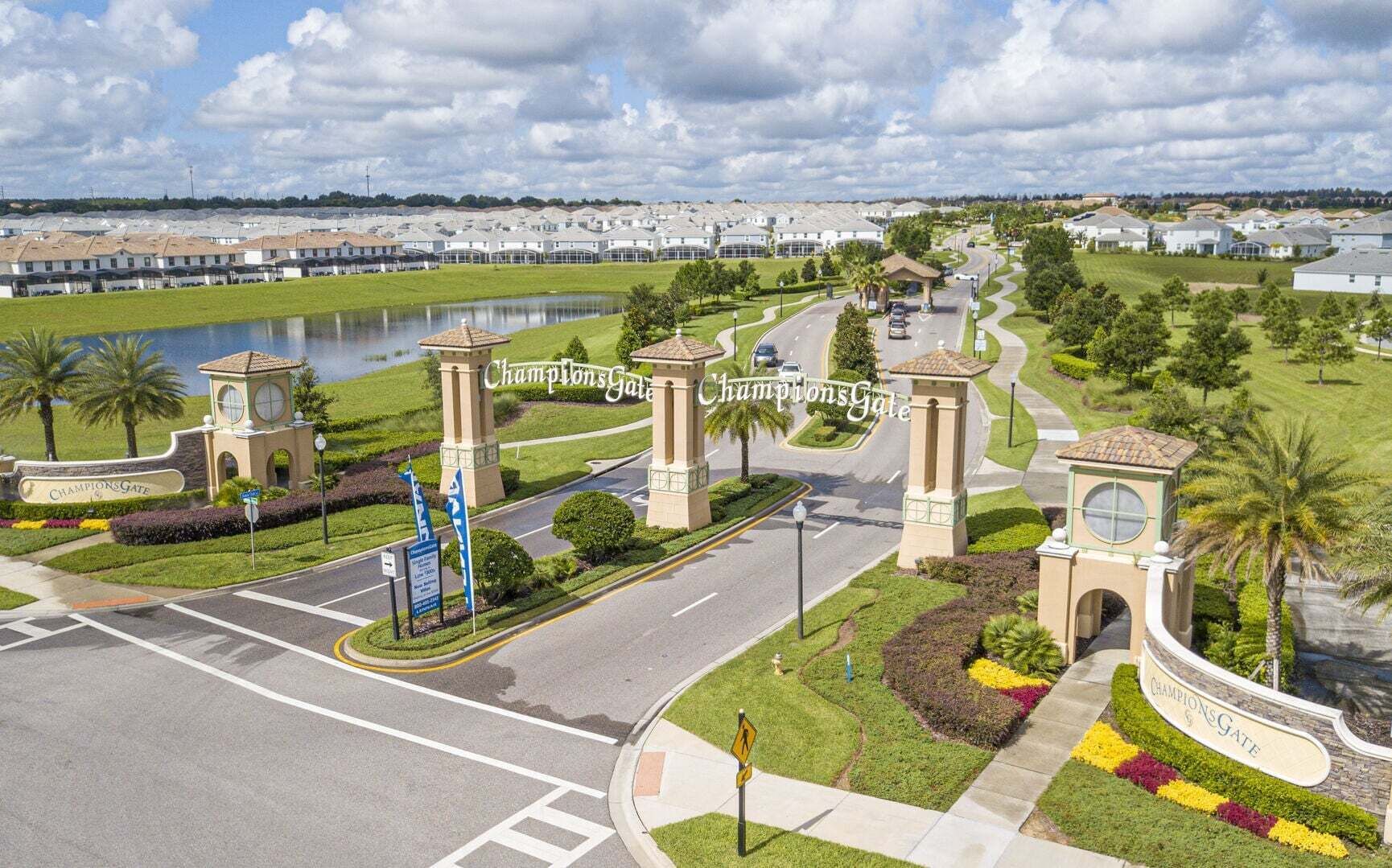 A gated community with a central road, landscaped areas, and a body of water.