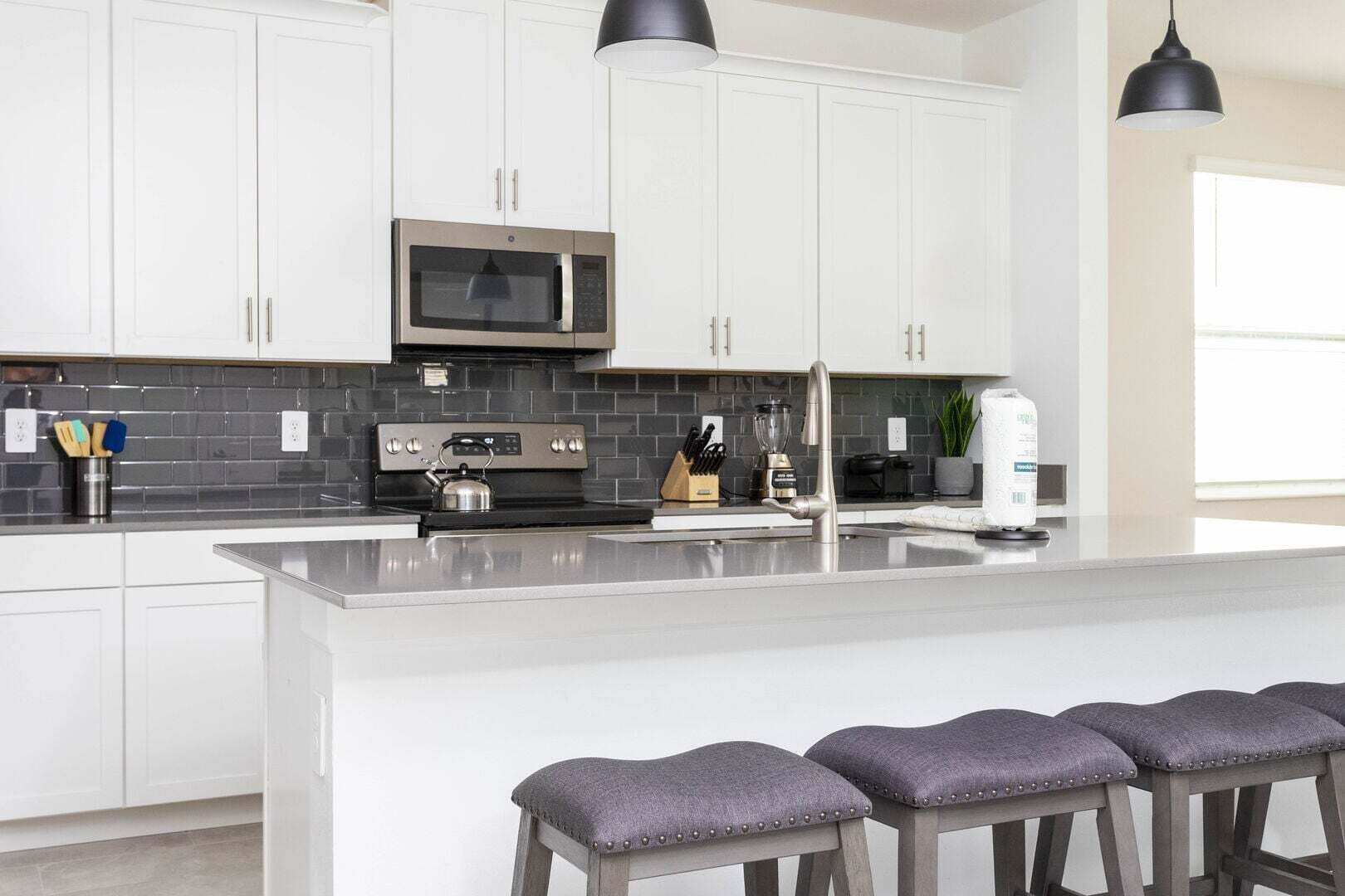 A modern kitchen with white cabinets, a central island with bar stools, a built-in microwave, and a black backsplash.