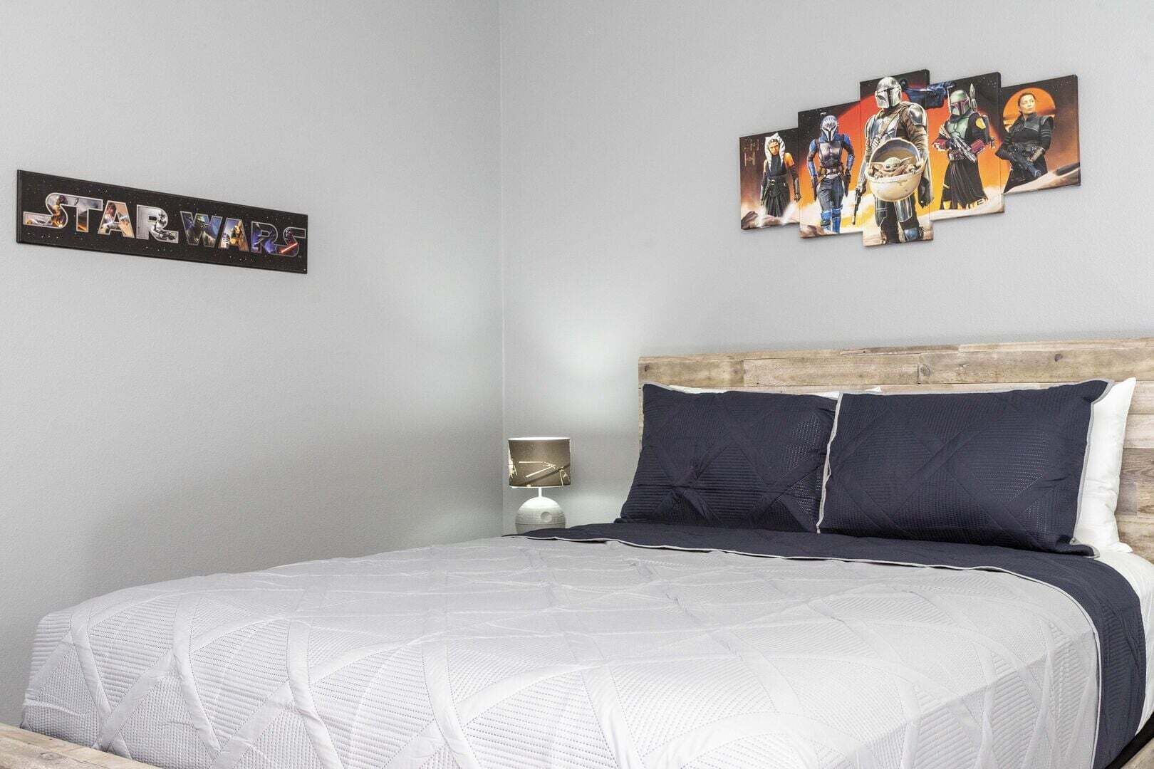 Ein Schlafzimmer mit einem Bett, Kissen, Wandkunst zum Thema Star Wars und einer Nachttischlampe.