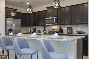 A modern kitchen with dark cabinets, stainless steel appliances, and a central island with bar stools. - Modern Vacation Home 5 BR, 4.5 BA Villa Sleeps 12! (Davenport)