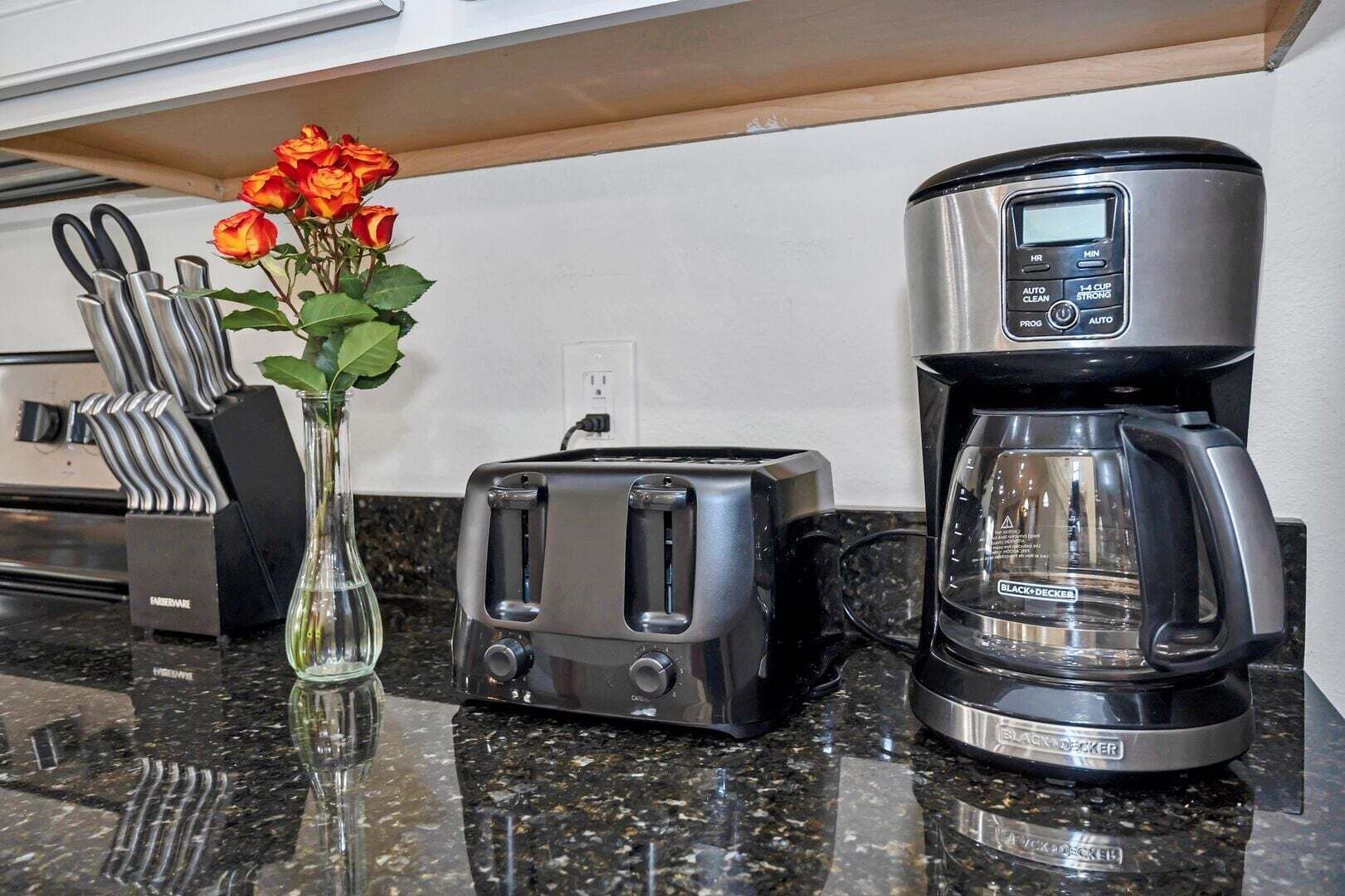 A kitchen with a toaster, coffee maker, and a vase with flowers on a granite countertop.