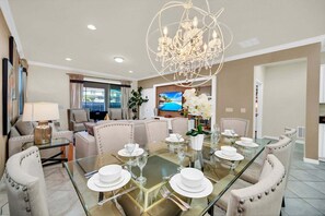 A dining area with a glass table set for six, surrounded by upholstered chairs. - Glamorous Home, Private Pool Sleeps 14 Ww103 (Kissimmee)
