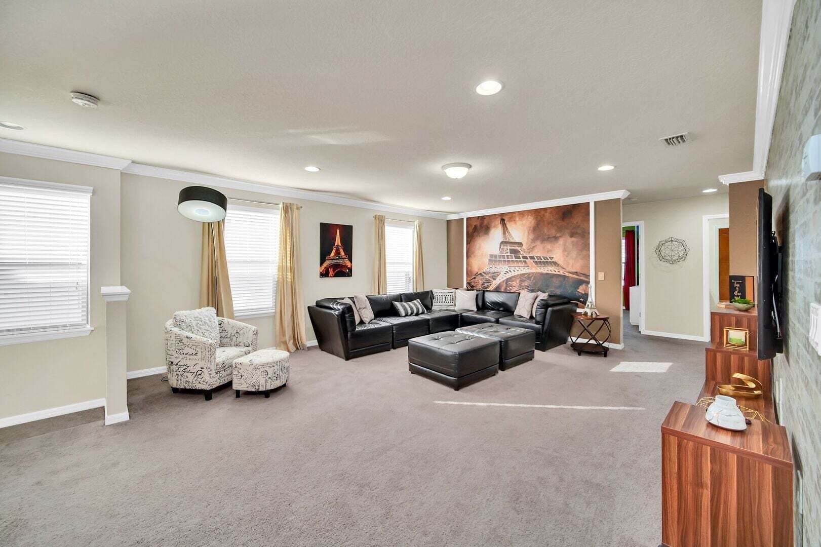 A living room with a sectional sofa, ottomans, a patterned armchair, and a large wall mural.