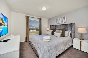Ein Hotelzimmer mit Bett, Fernseher, Schreibtisch, Nachttisch und einem Fenster mit Vorhängen.