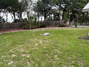 A grassy backyard with a wooden fence, trees, and a stone. - Waterfront Canal/Park Your Boat (Homosassa)