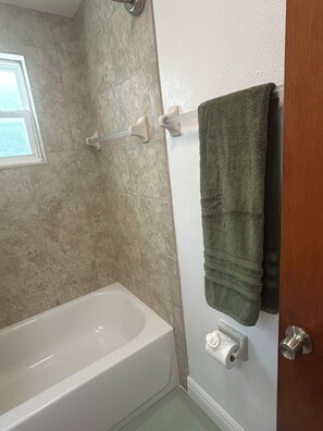 Une salle de bain avec une baignoire, un porte-serviettes avec une serviette verte et un porte-rouleau de papier toilette.