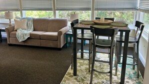A room with a beige sofa, a dining table with chairs, a ceiling fan, and large windows with blinds. - Waterfront Canal/Park Your Boat (Homosassa)