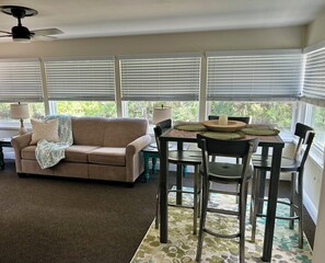 A room with a beige sofa, a dining table with chairs, a ceiling fan, and large windows with blinds. - Waterfront Canal/Park Your Boat (Homosassa)