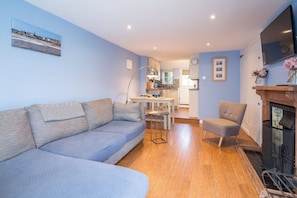 A living room with a sofa, a chair, a dining table, and a kitchen in the background. - The Little Blue House, Southwold (Southwold)