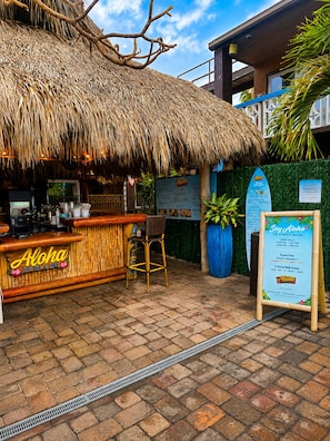 A thatched-roof bar area with a menu board, a seating area, and a paved walkway.