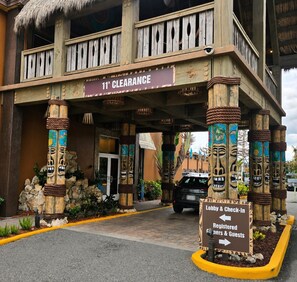 A building with a 11' clearance sign, tiki-themed pillars, and a sign directing to the lobby and check-in for registered guests.