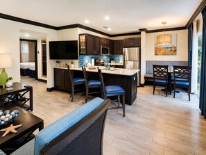 A modern kitchen with dark wood cabinets, a central island, and a dining area with blue chairs. - PRICE DROP! 2BR Resort Villa, Pool, Splash Pad, Gym & Shuttle. Great for family. (Cocoa Beach)