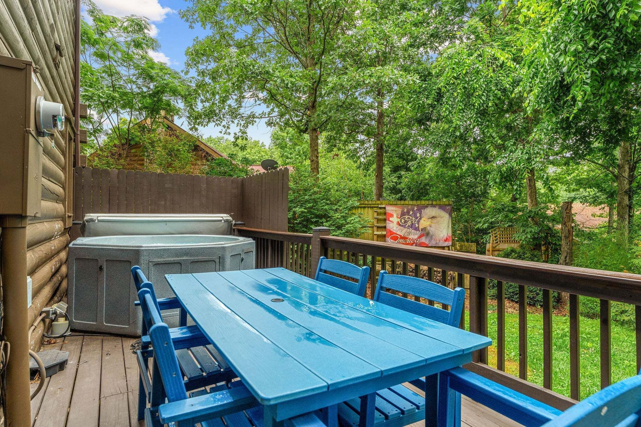 A wooden deck with a blue table and chairs, a hot tub, and a wooden fence.