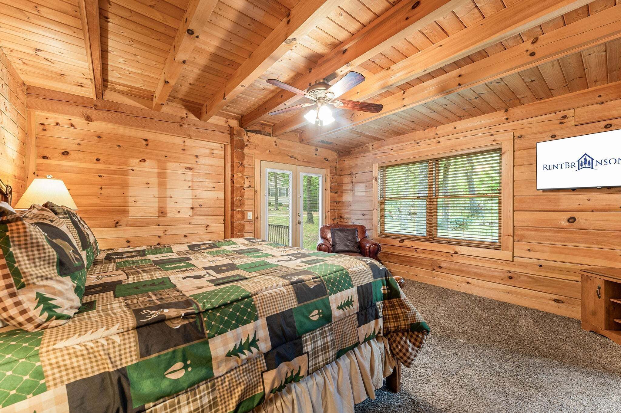 A log cabin bedroom with a bed, a chair, a ceiling fan, and a window.