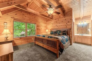 A wooden cabin bedroom with a bed, two bedside lamps, a ceiling fan, and a large window. - Authentic Log Cabin Mins to Thunder Ridge&Big Cedar_Free Attraction Tickets_Pvt Hot Tub_Pool Table (Hollister)