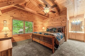 A wooden cabin bedroom with a bed, a nightstand, a lamp, a ceiling fan, and a window with blinds. - Authentic Log Cabin Mins to Thunder Ridge&Big Cedar_Free Attraction Tickets_Pvt Hot Tub_Pool Table (Hollister)