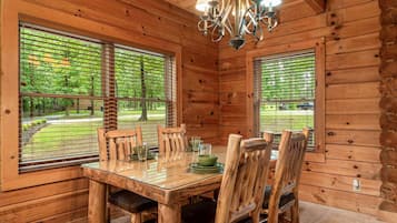 A wooden cabin interior with a dining table, chairs, and a chandelier.