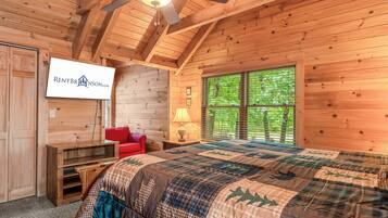 A wooden cabin interior with a bed, a TV, a window with blinds, and a ceiling fan.