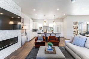 Ein modernes Wohnzimmer mit Kamin, Sofa, Hocker und Essbereich.