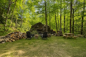 Ein bewaldeter Campingplatz mit zwei Adirondack-Stühlen, einem Picknicktisch und einer großen Felsformation.