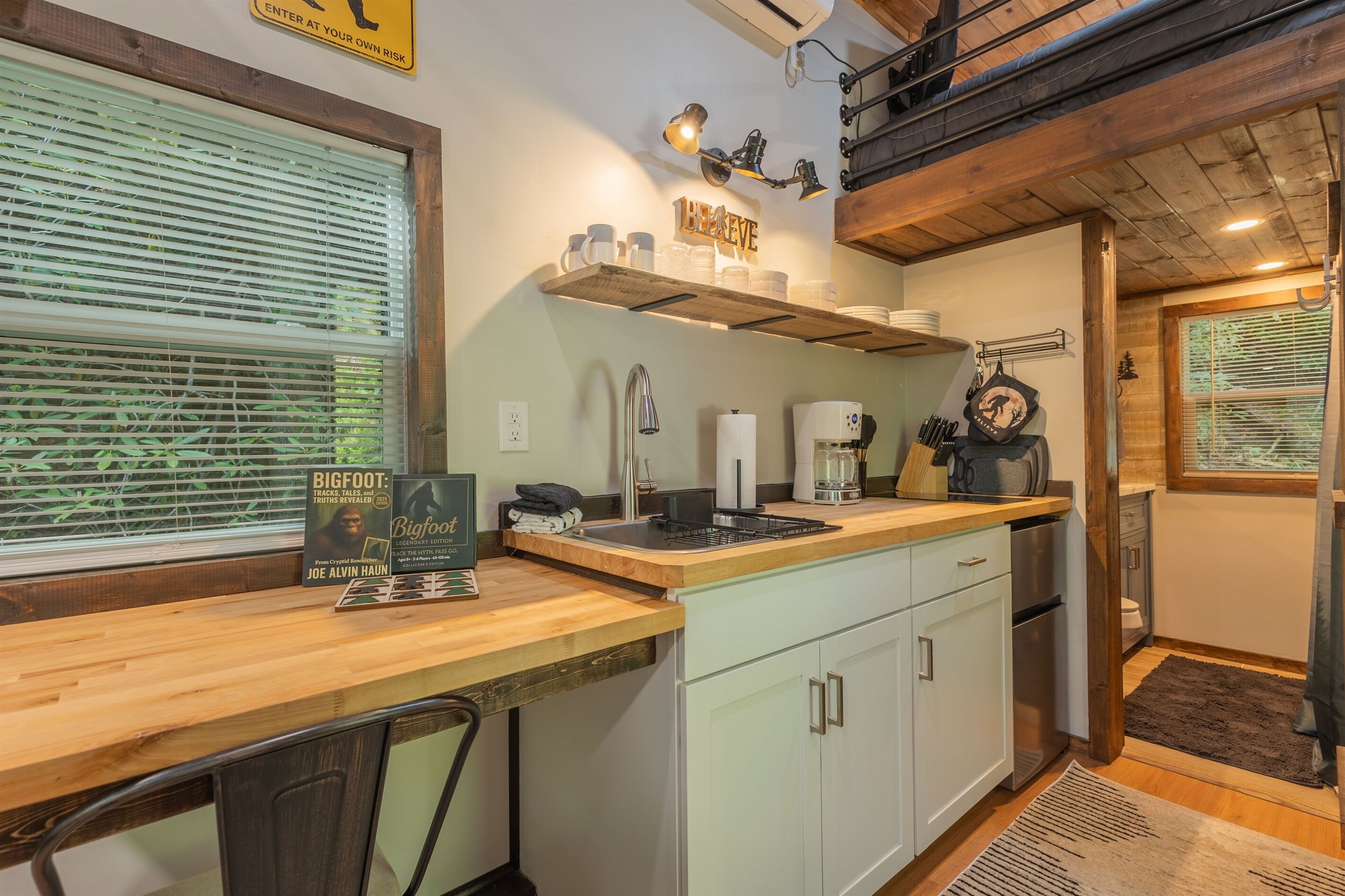 A kitchen with a wooden countertop, white cabinets, a coffee maker, and a sign that says 'BE AWARE'.