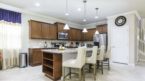 Una cucina con mobili in legno, un frigorifero in acciaio inox, un forno a microonde e una sveglia appesa al muro.