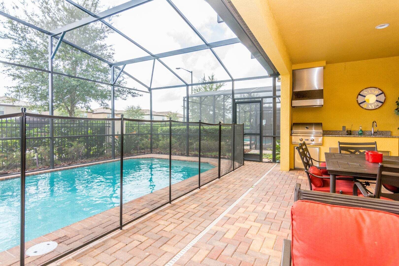 Ein Schwimmbad mit Glasveranda, eine Terrasse mit Tisch und Stühlen sowie eine Küchenzeile mit Herd und Spüle.