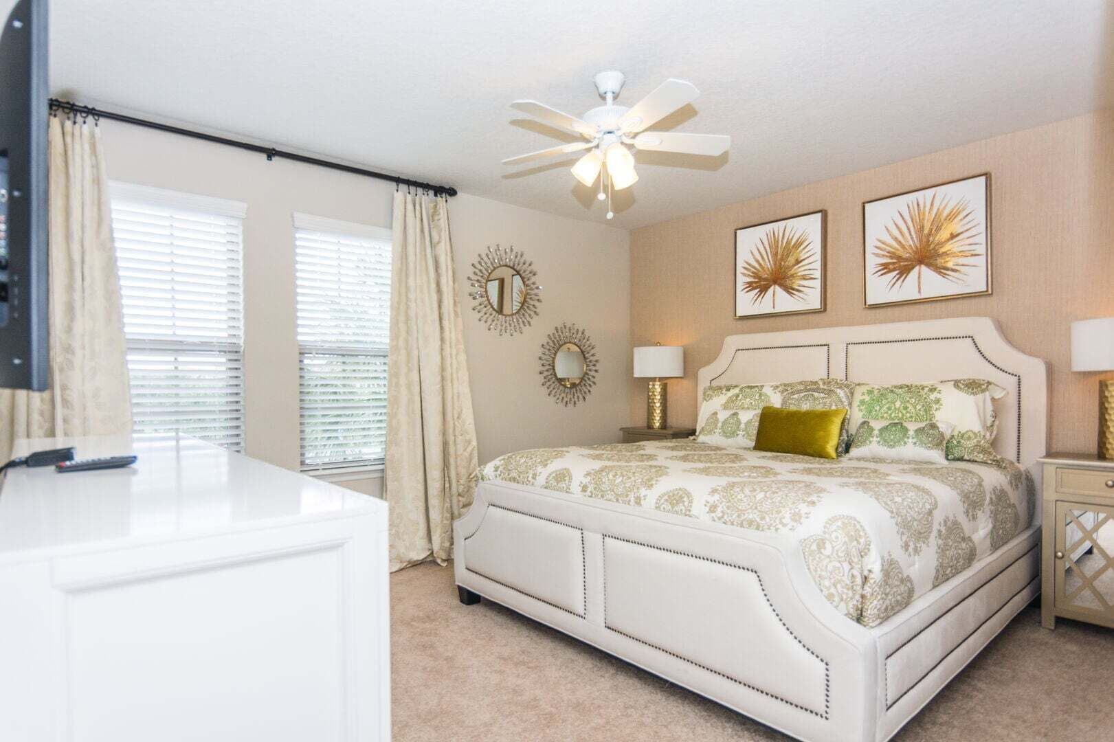Un dormitorio con cama, ventilador de techo, decoración en la pared y televisor.