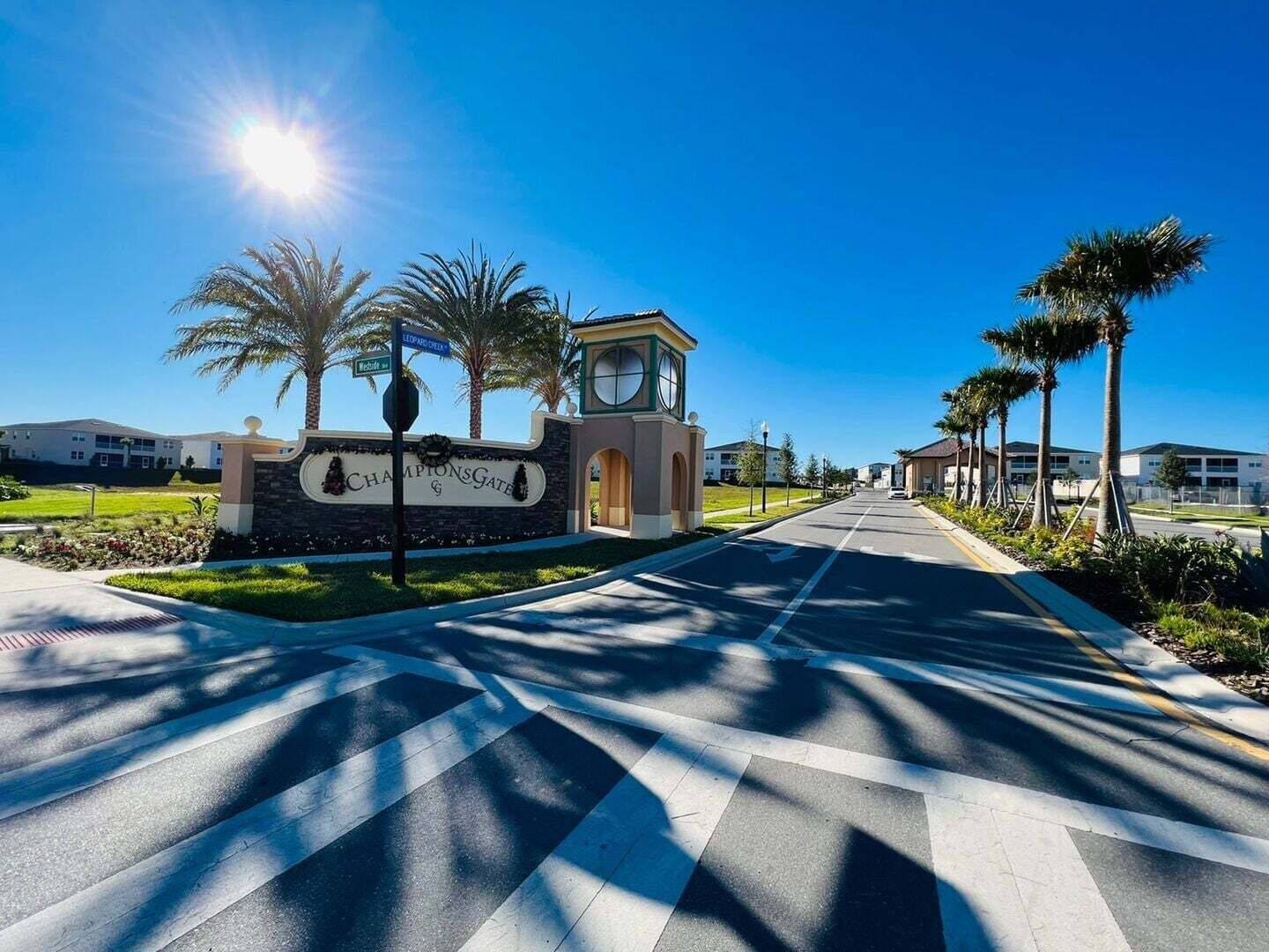 A street leading to a gated community with a clear sky and palm trees.