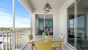 A balcony with a glass table and chairs, a hanging light fixture, and a view of a parking area and buildings. - Free Water Park Walking Distance! (Davenport)