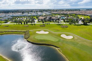 Vista aerea di un campo da golf con bunker di sabbia, uno stagno e una zona residenziale sullo sfondo.