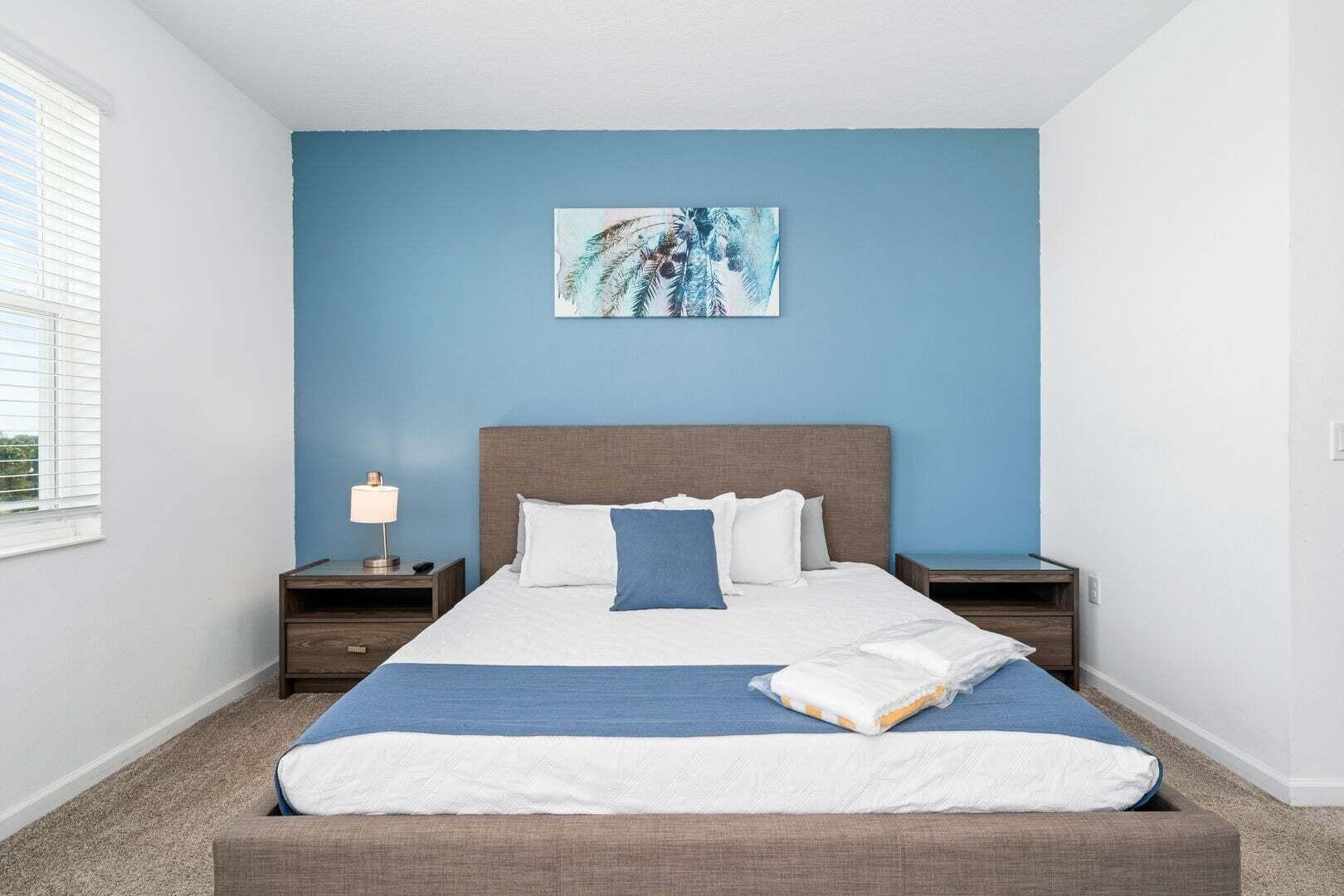 Een slaapkamer met een bed, nachtkastje, lamp en een schilderij aan de muur.