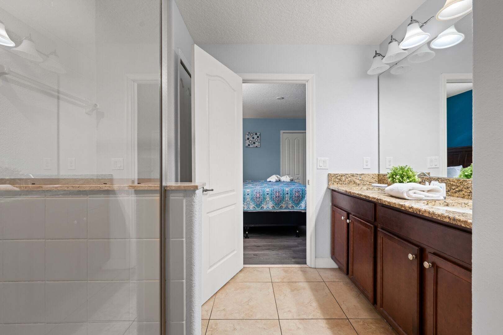 A bathroom with a shower, a sink with a granite countertop, and a mirror.