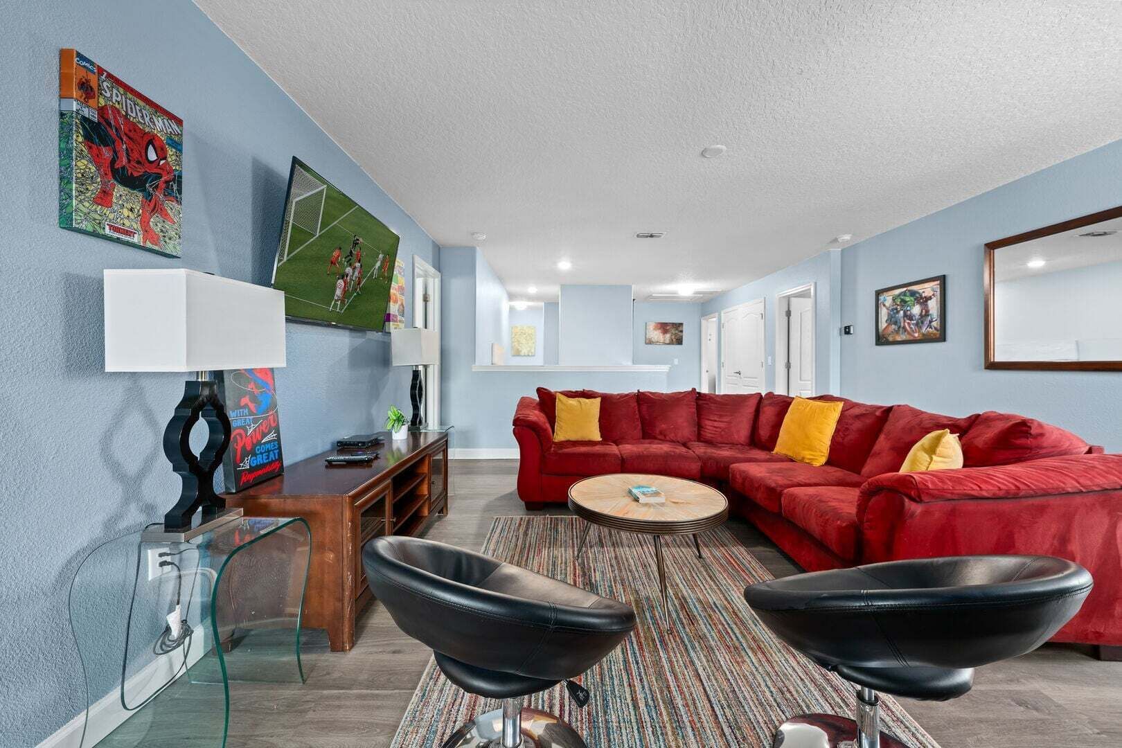 A living room with a red sectional sofa, a glass coffee table, a black leather chair, a wooden side table, a lamp, and a wall-mounted TV.