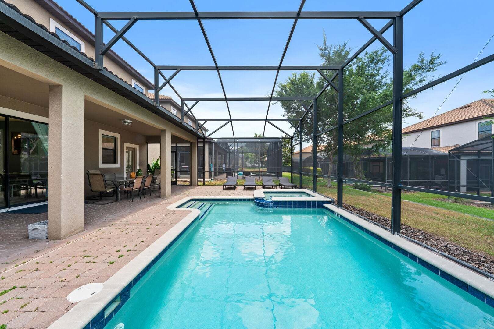 A swimming pool with a covered patio area, outdoor seating, and a view of neighboring houses.