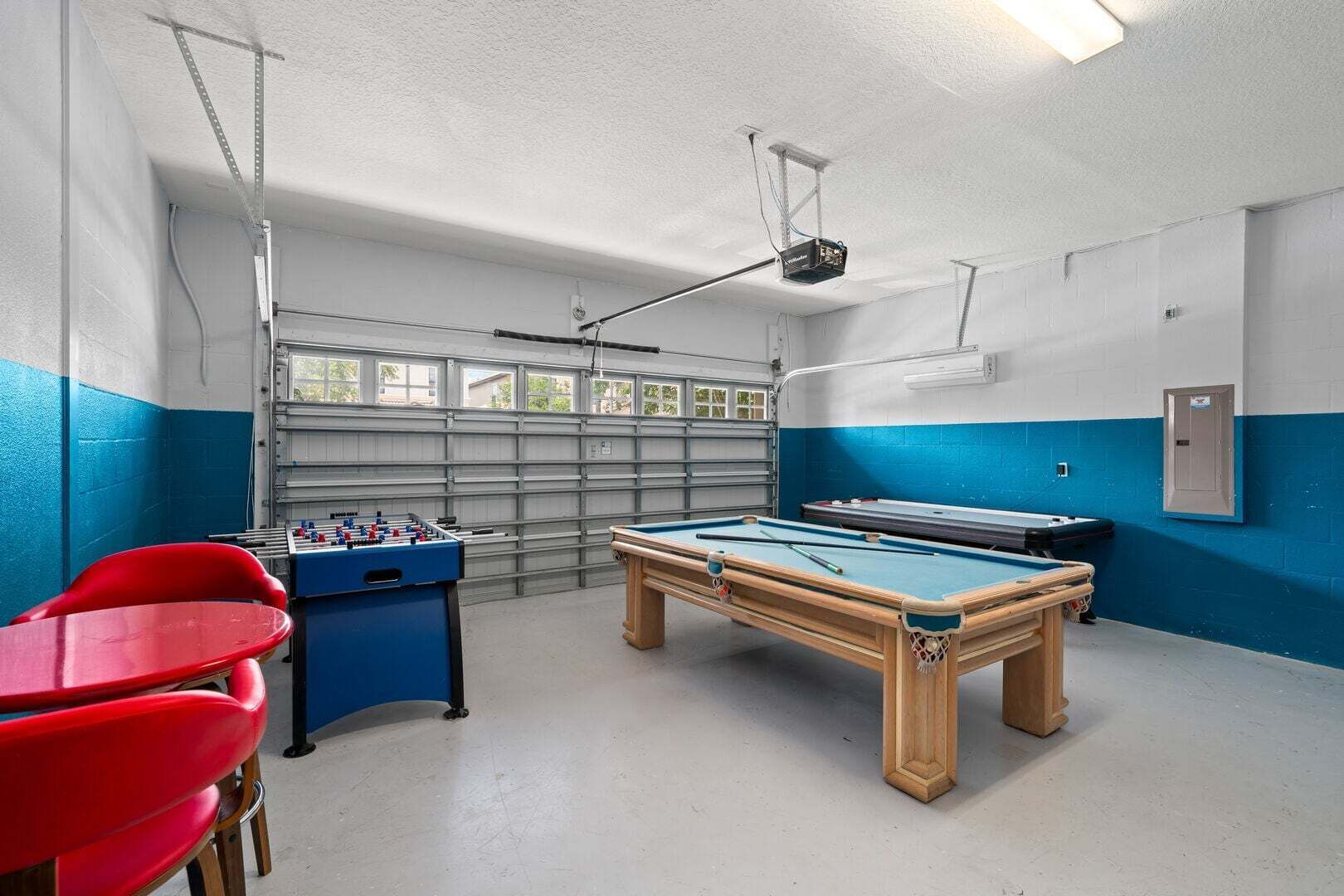 A recreational room with a pool table, foosball table, and red chairs.