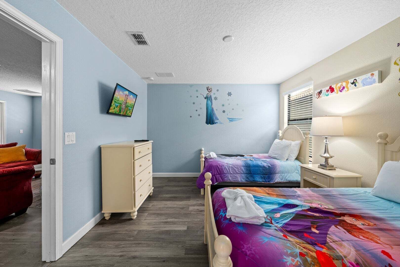 Quarto com duas camas, uma cômoda, uma cadeira vermelha e uma parede com mural.