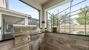A kitchen with a stainless steel grill, dark wood cabinetry, and large windows offering a view of the outdoors. - Spacious 9br, 9BA Resort Home w/ Private Pool (Kissimmee)