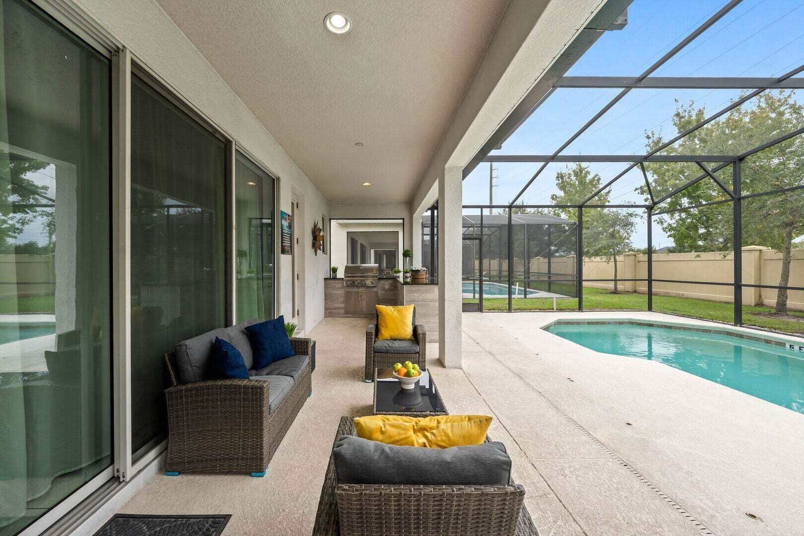 A covered outdoor area with a pool, wicker furniture, and a view of the backyard.