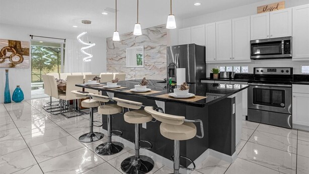 A modern kitchen with a central island, bar stools, stainless steel appliances, and pendant lighting. - Spacious 9br, 9BA Resort Home w/ Private Pool (Kissimmee)