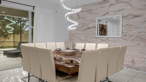 A modern dining area with a marble wall, a large round table, and white upholstered chairs. - Spacious 9br, 9BA Resort Home w/ Private Pool (Kissimmee)