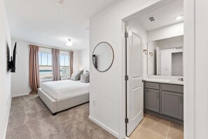 Ein Schlafzimmer mit Bett, ein Badezimmer mit Waschbecken und Spiegel sowie Blick auf den Strand.